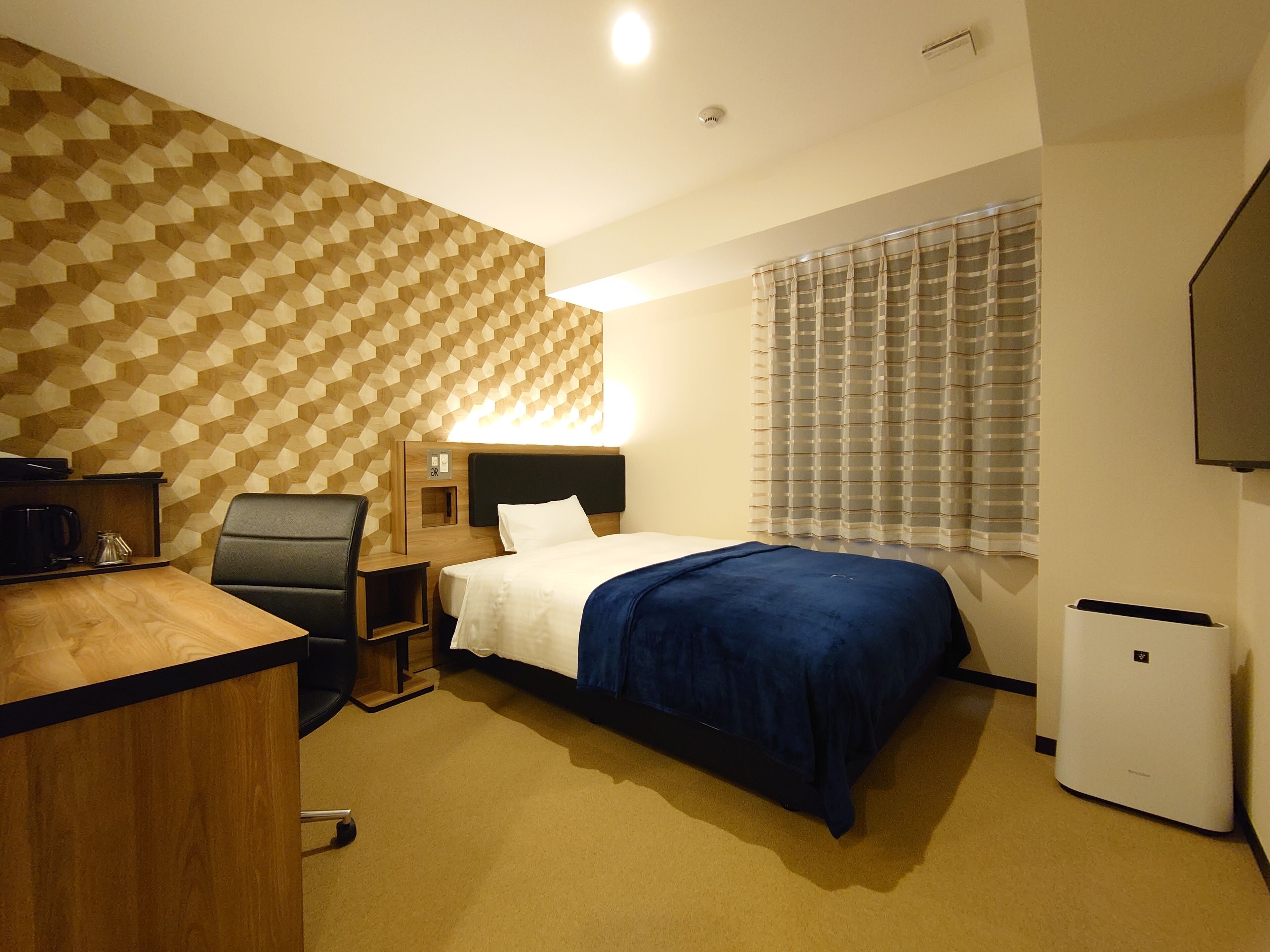 A hotel room with a bed, a desk, a chair, a coffee maker, and a TV.