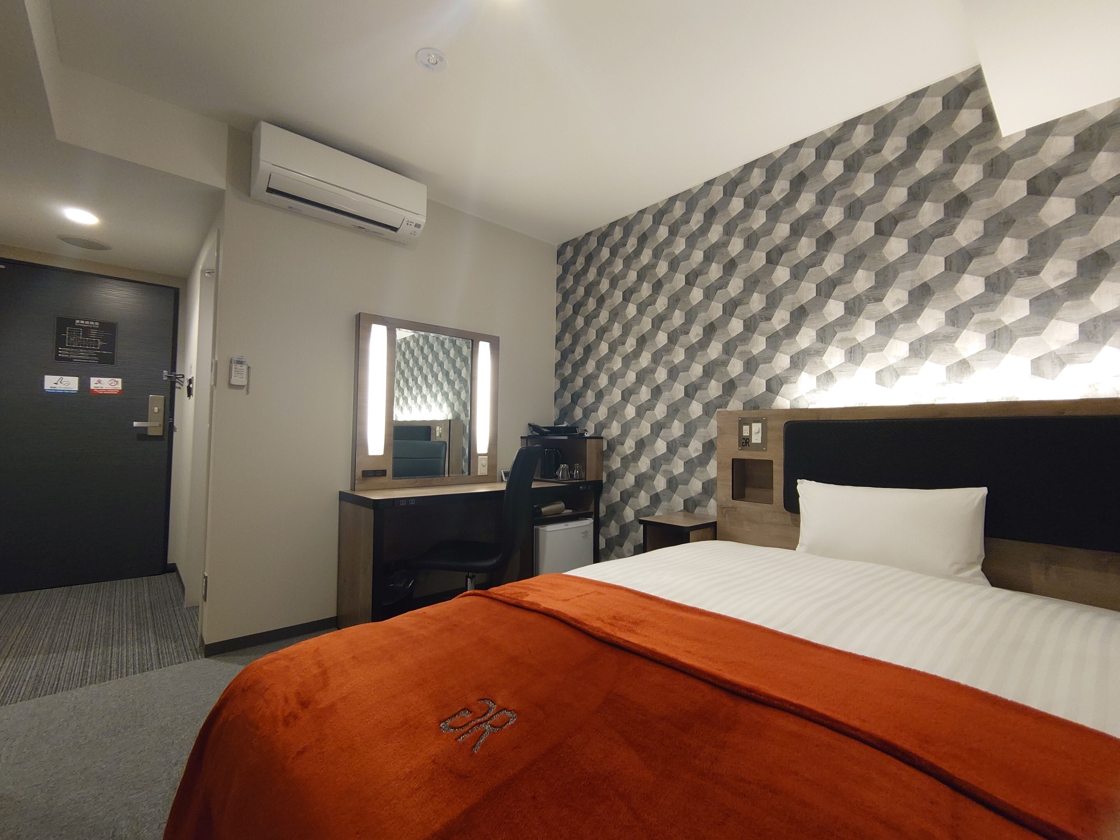 Een hotelkamer met een bed, een bureau, een stoel, een airconditioning en een behang met patroon.
