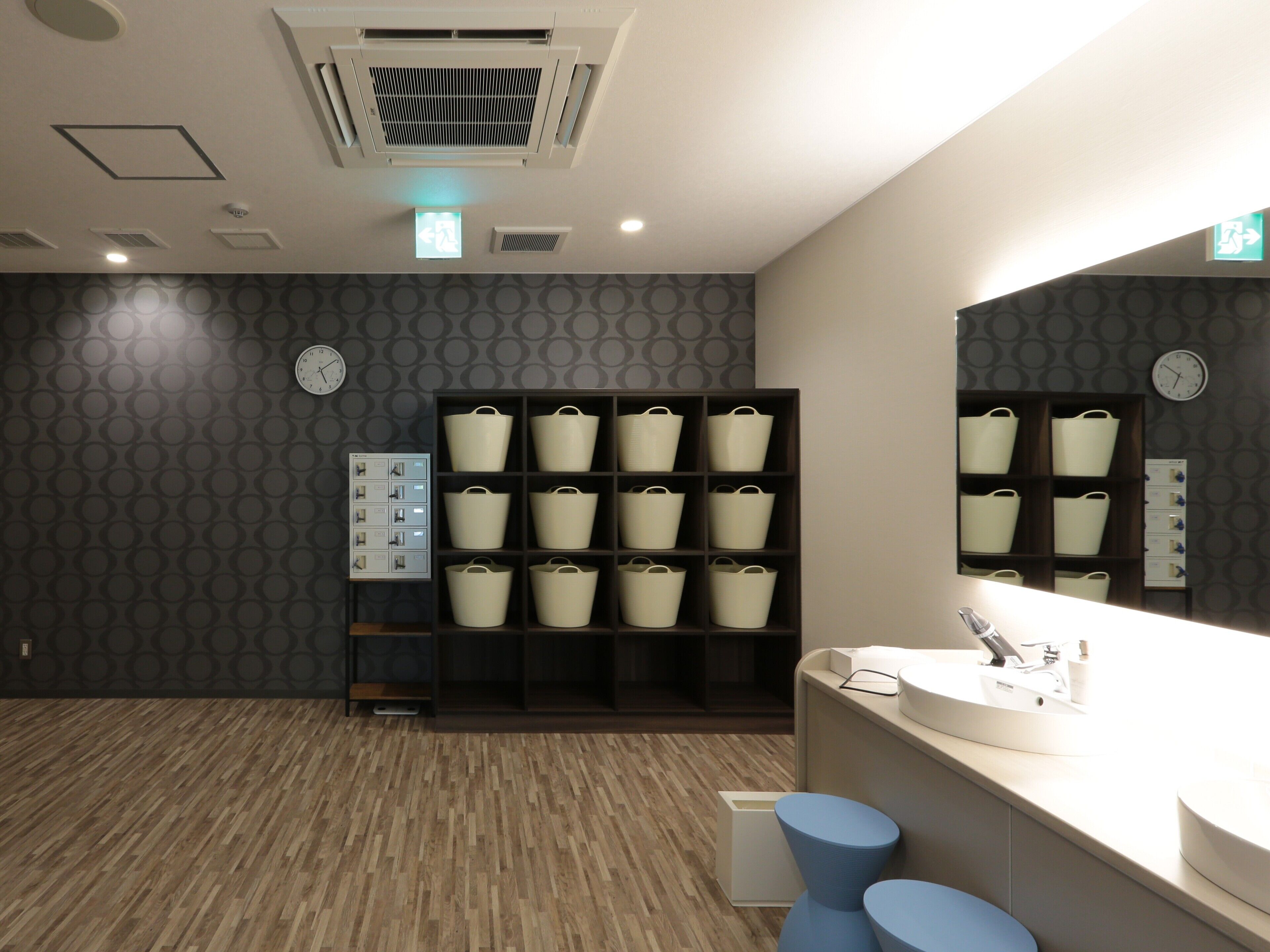 A modern bathroom with a wooden floor, a sink with a mirror, and storage baskets on shelves.