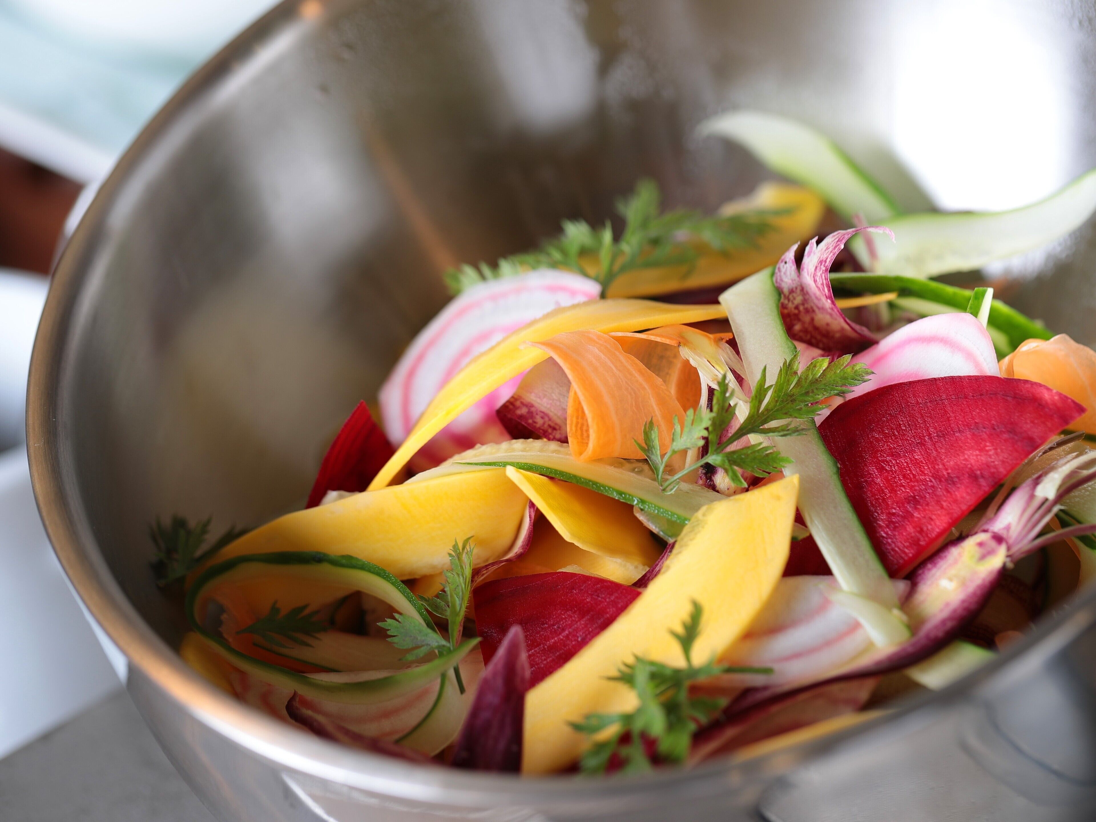 A stainless steel bowl filled with sliced fruits and vegetables, garnished with parsley.
