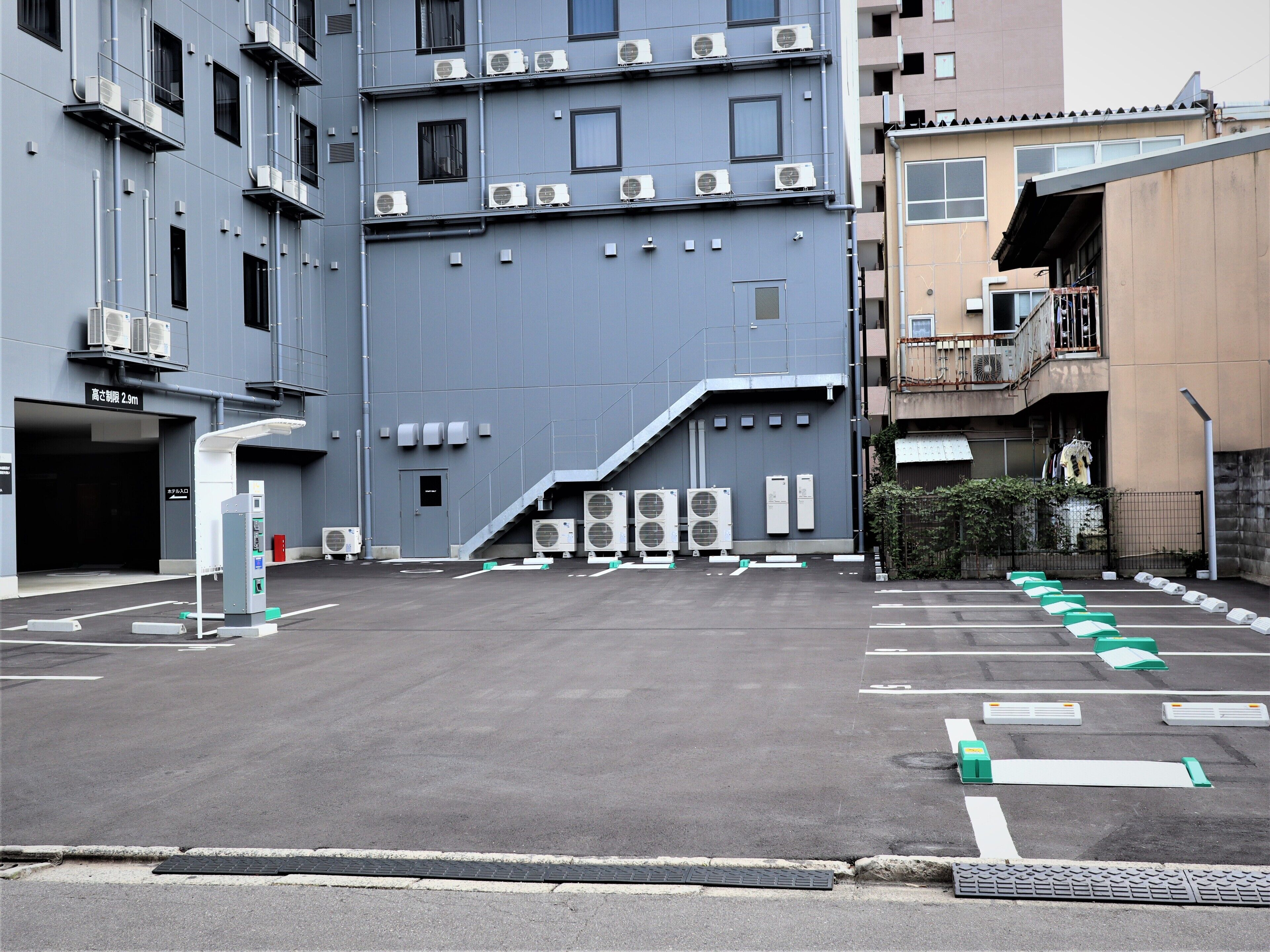 A parking lot with multiple air conditioning units, a gas station, and a building with a staircase leading to an upper level.
