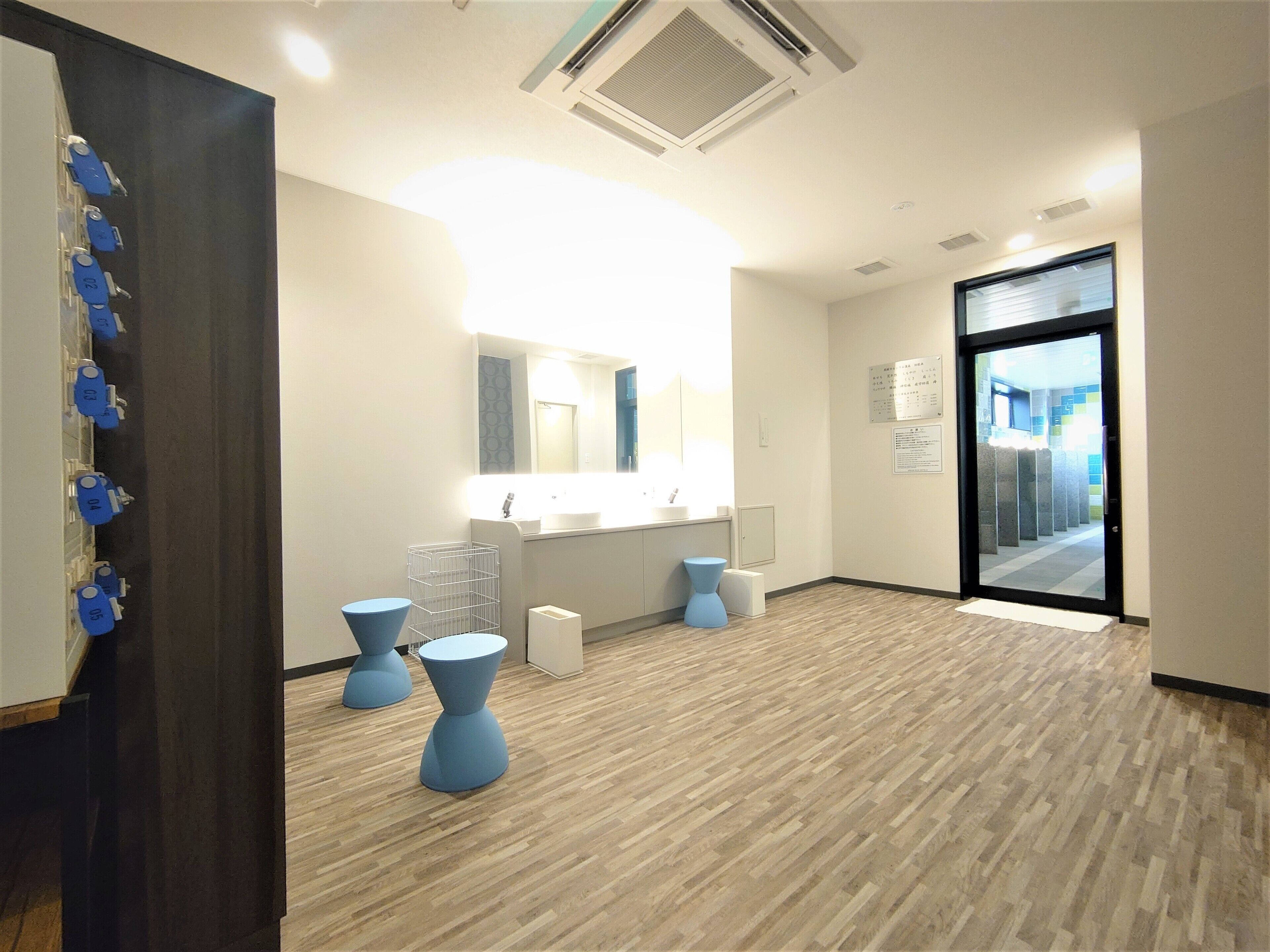 Un moderno vestíbulo de hotel con piso de madera, un espejo grande, una recepción y una puerta de vidrio que da al exterior.