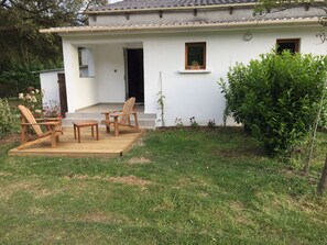 Una casa blanca con terraza de madera, dos sillas de madera y una pequeña mesa.