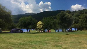 Un terrain de camping avec des tentes et des arbres, situé dans un cadre magnifique avec des montagnes en toile de fond et un ciel dégagé.