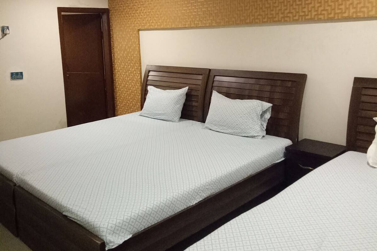 A hotel room with two beds, a wooden headboard, a patterned wall, and a door.