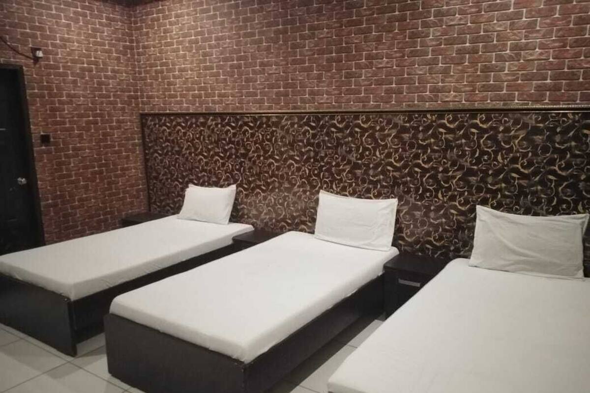 A room with three single beds aligned against a brick wall with a decorative headboard.