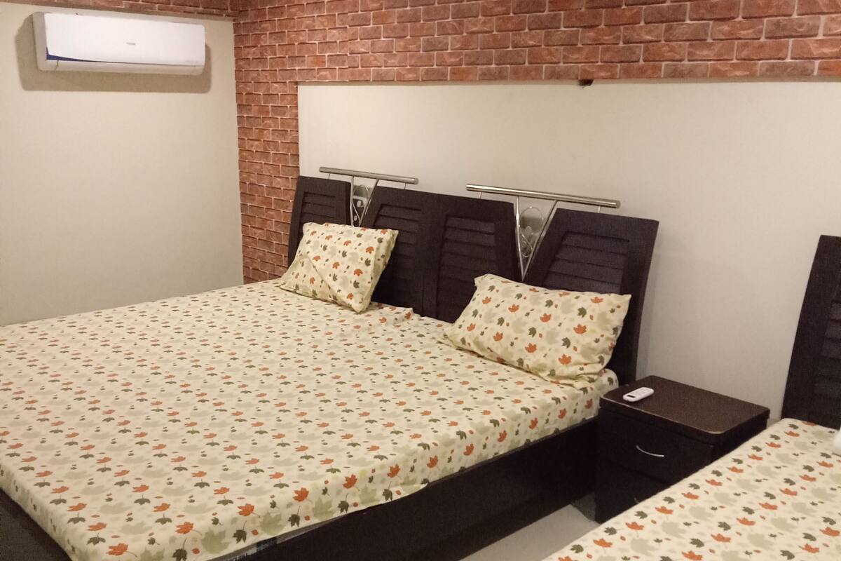 A bedroom with two beds, a brick wall, and a ceiling light.