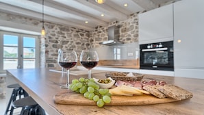 Un comptoir de cuisine sur lequel se trouve une planche à découper en bois, avec des raisins, du fromage et du pain. On peut également apercevoir deux verres de vin rouge.