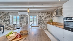 Une cuisine aux murs en pierre, avec un îlot central en bois doté d’un évier et un four Bosch.