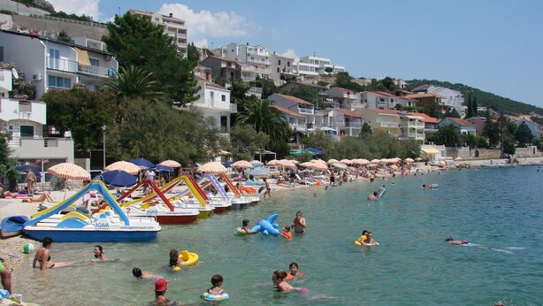 Een strand met helder water, parasols en mensen die zwemmen en ontspannen.