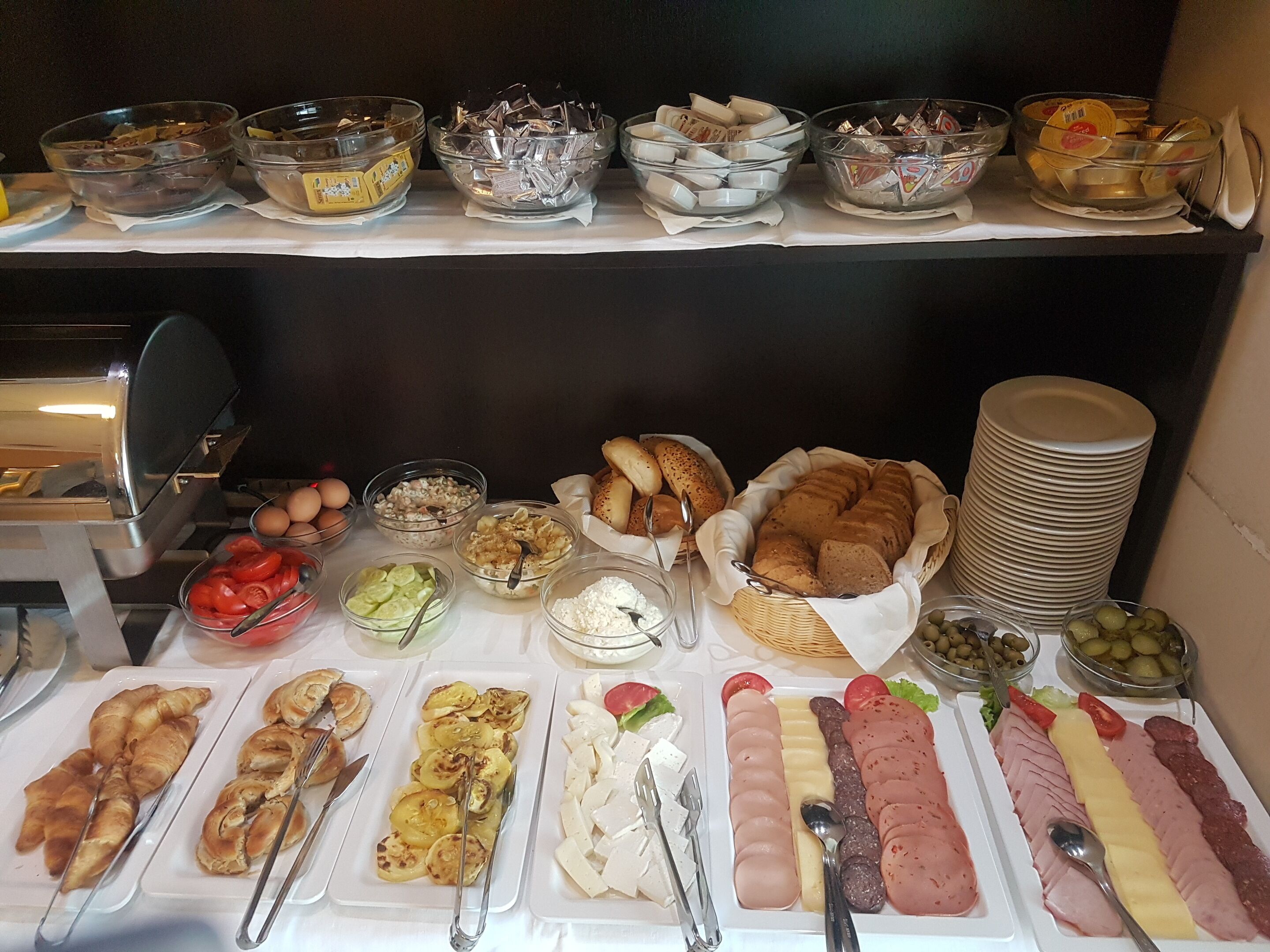 Een buffet met diverse gerechten, waaronder brood, vleeswaren, kazen en groenten.