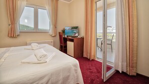 Een hotelkamer met een bed, een bureau met een computer, een televisie en uitzicht op de zee door een schuifdeur.