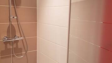 Une salle de bain avec des murs recouverts de carreaux beiges, une douche équipée d’un pommeau de douche à main et un sol blanc.