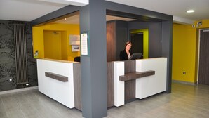Un área de recepción con diseño moderno, que incluye un mostrador de recepción, un panel informativo en la pared y una puerta que da a otra habitación.