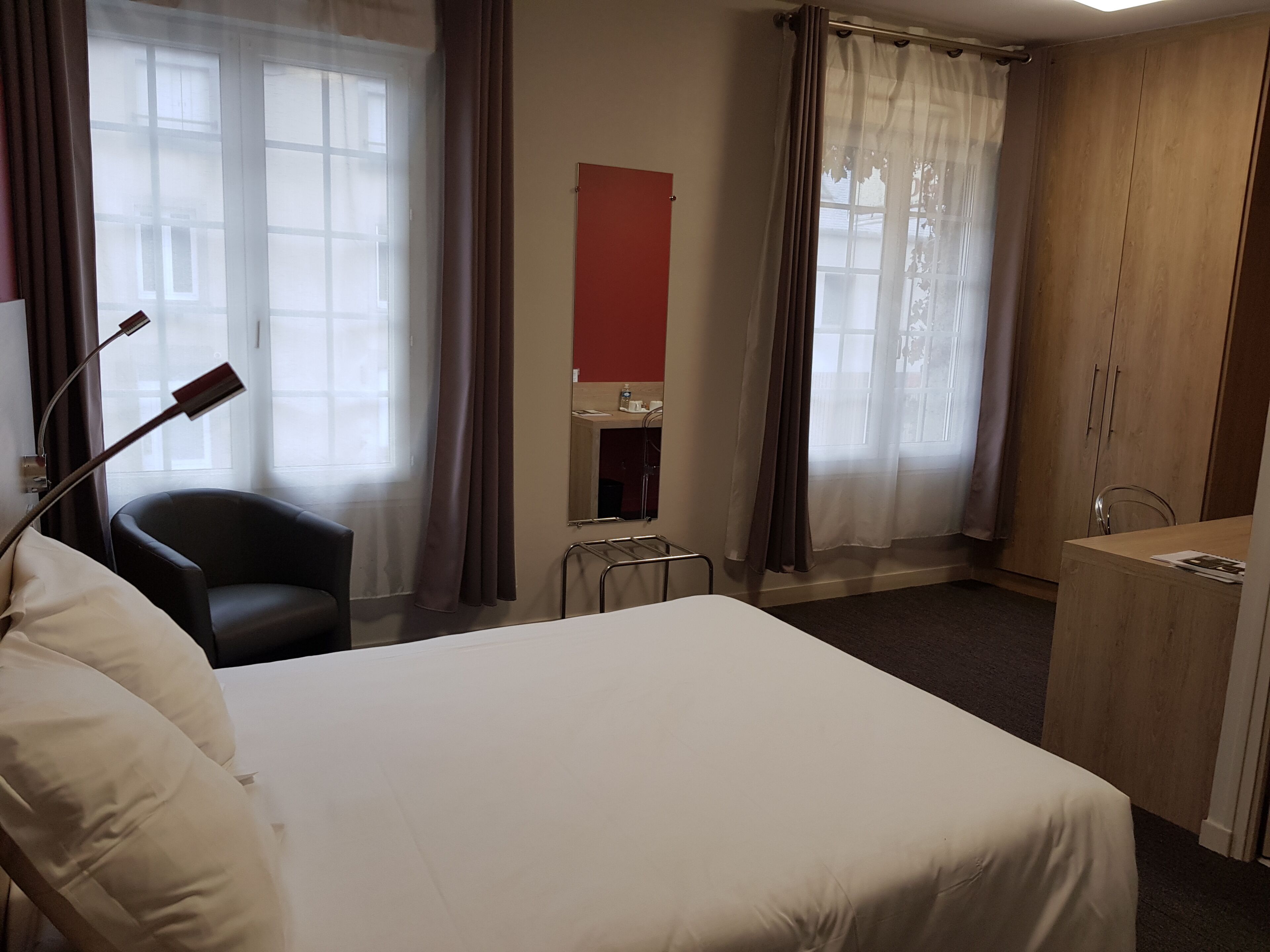 A hotel room with a bed, a chair, a desk, and a mirror.