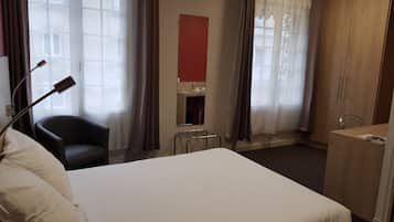 A hotel room with a bed, a chair, a desk, and a mirror.