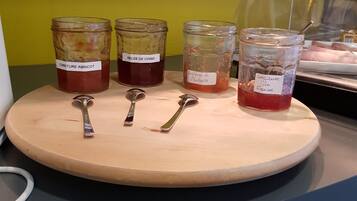 A wooden board with four glass jars labeled with different types of preserves, each with a spoon in front.