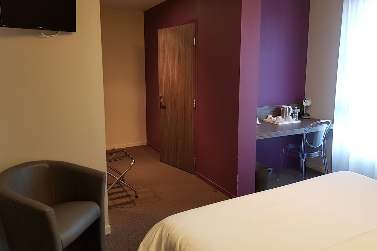Habitación de hotel con cama, escritorio con silla, televisor montado en la pared y puerta que da a otra habitación.