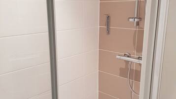 A shower area with white and beige tiles, a glass door, and a showerhead.