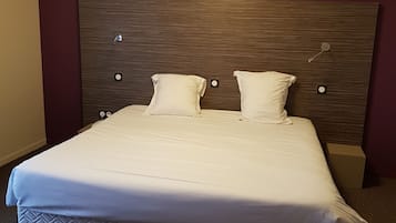 Een net opgemaakt bed met een houten hoofdbord, twee kussens en een witte deken.