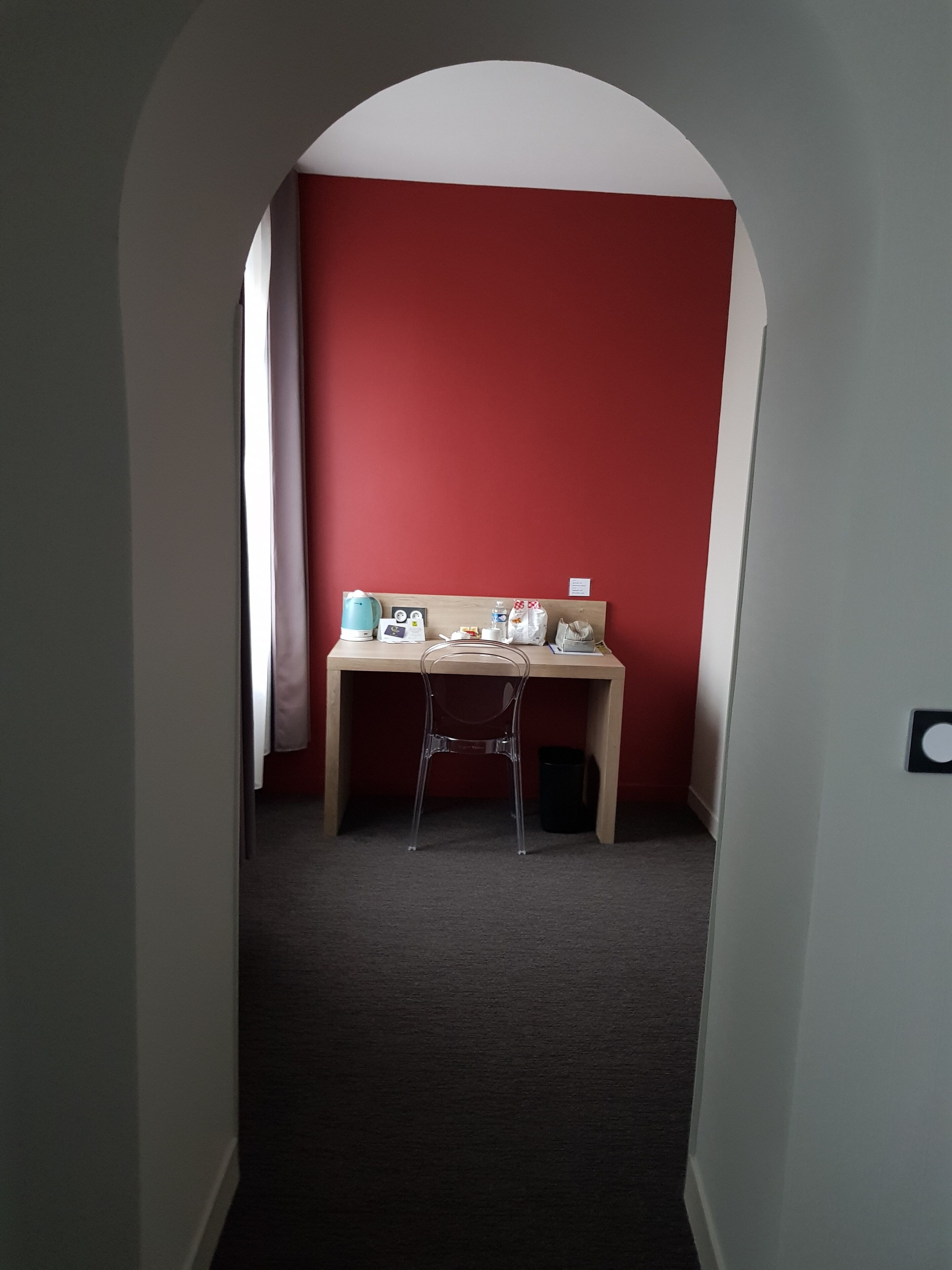 Un couloir étroit avec un bureau et une chaise, dans une pièce aux murs rouges.
