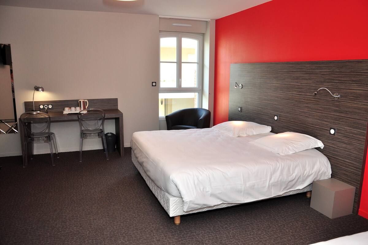 Una habitación de hotel con cama, escritorio, silla, cubo de basura y ventana.