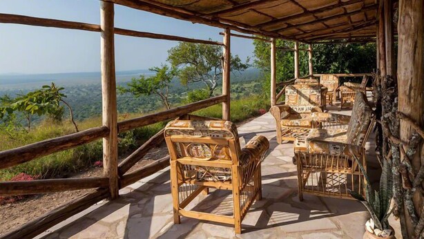 A wooden deck with wicker furniture overlooking a scenic landscape. - Eagles Nest Camp (Mbarara)