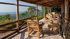 A wooden deck with wicker furniture overlooking a scenic landscape. - Eagles Nest Camp (Mbarara)