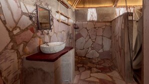 A stone-walled bathroom with a marble sink, a mirror, and a shower area. - Eagles Nest Camp (Mbarara)