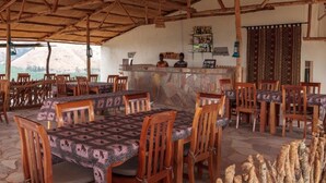 A restaurant with wooden tables and chairs, a stone wall, and a bar area. - Eagles Nest Camp (Mbarara)