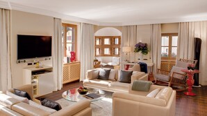 A spacious living room with a flat-screen TV, comfortable seating, a glass coffee table, and a view of the outside through large windows. - Giardino Bed & Breakfast (Silvaplana)