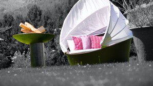 A wicker chair with a white canopy, pink cushions, and a green base, placed outdoors with a hilly landscape in the background. - Giardino Bed & Breakfast (Silvaplana)