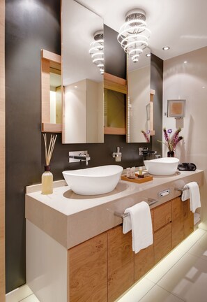 Un baño moderno con dos lavamanos grandes, un espejo y una araña.