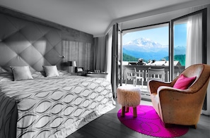 A modern bedroom with a large bed, a chair, a small stool, and a view of mountains through a balcony. - Giardino Bed & Breakfast (Silvaplana)