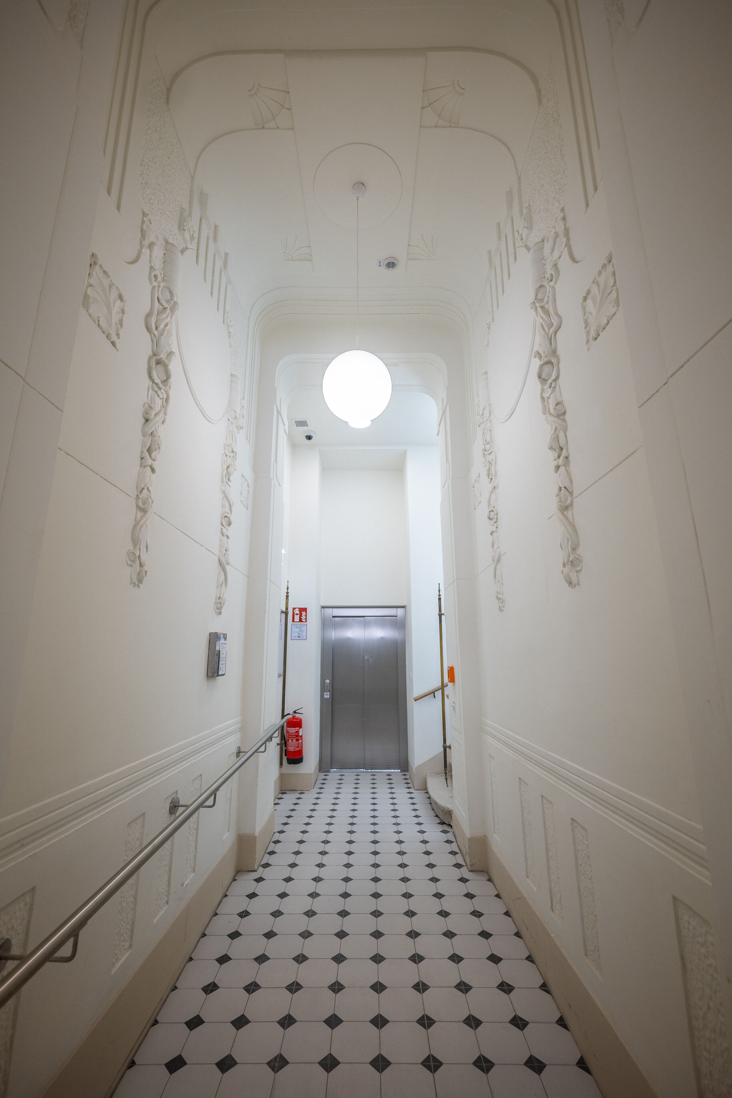 En hall med ett klinkergolv, ett ledstång och en dörr längst ner.