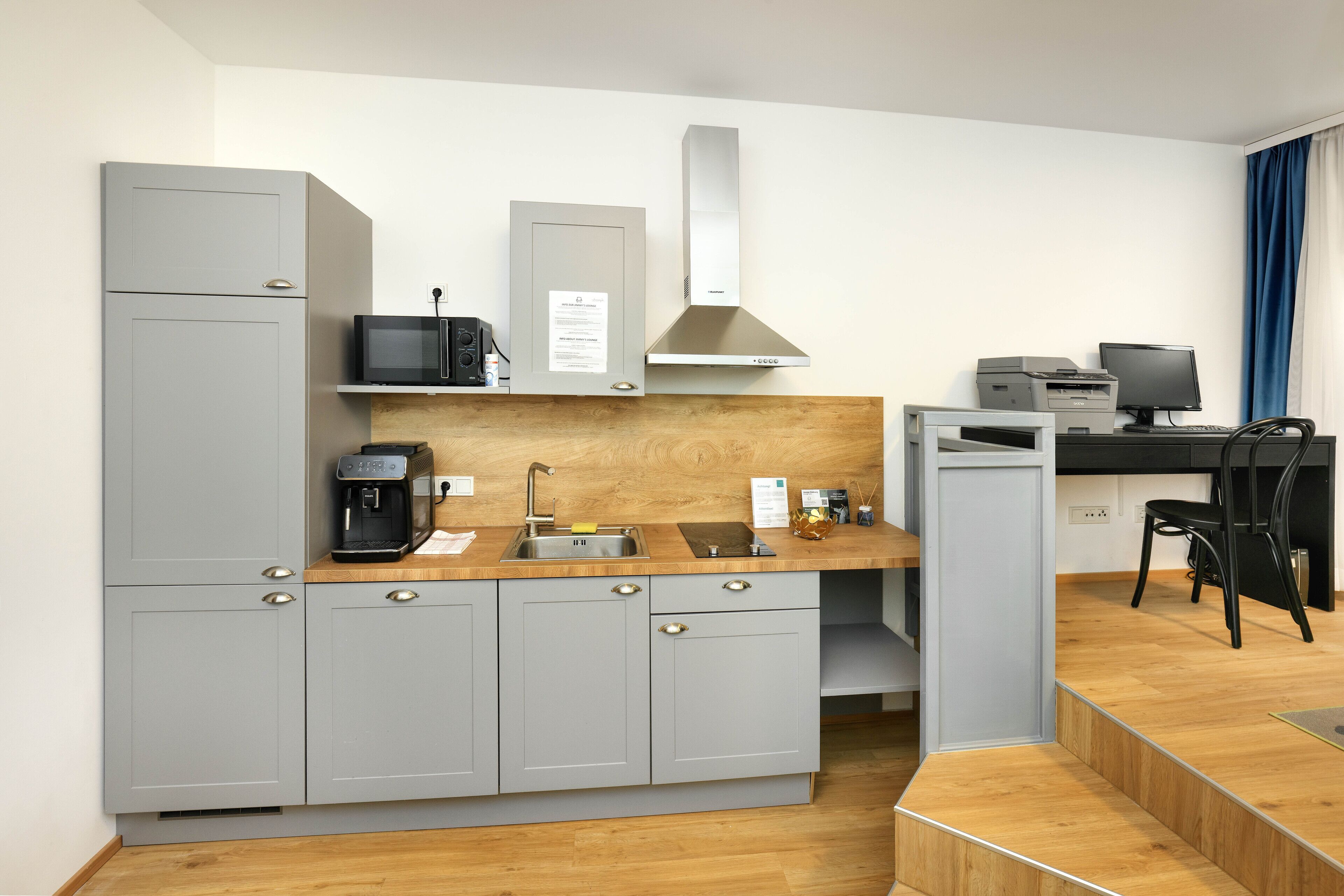 Eine moderne Küche mit grauen Schränken, einer Holzausziehtafel, einer eingebauten Mikrowelle, einer Kaffeemaschine und einer Edelstahl-Dunstabzugshaube.
