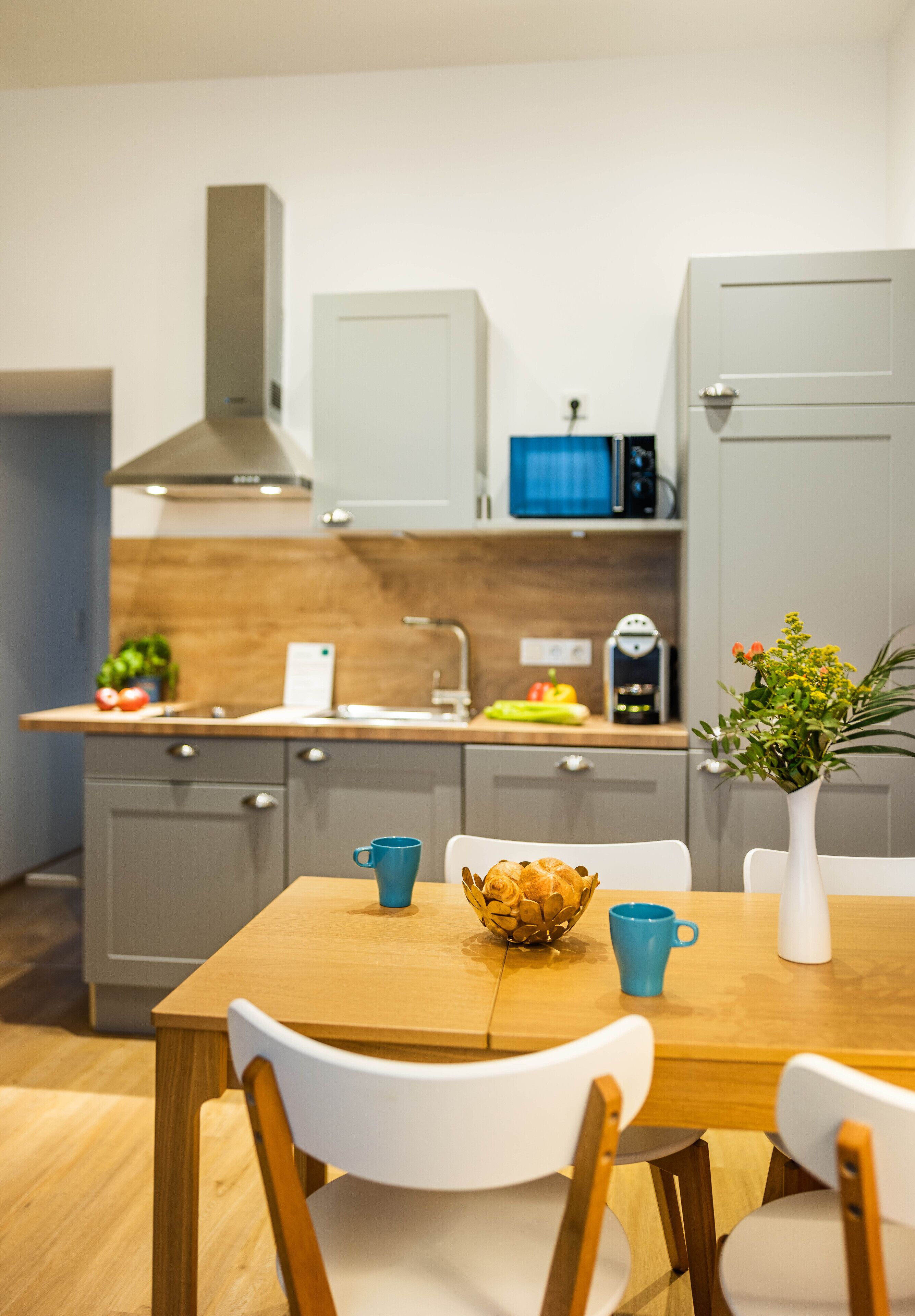 A modern kitchen with grey cabinets, a wooden countertop, and a dining table with chairs.