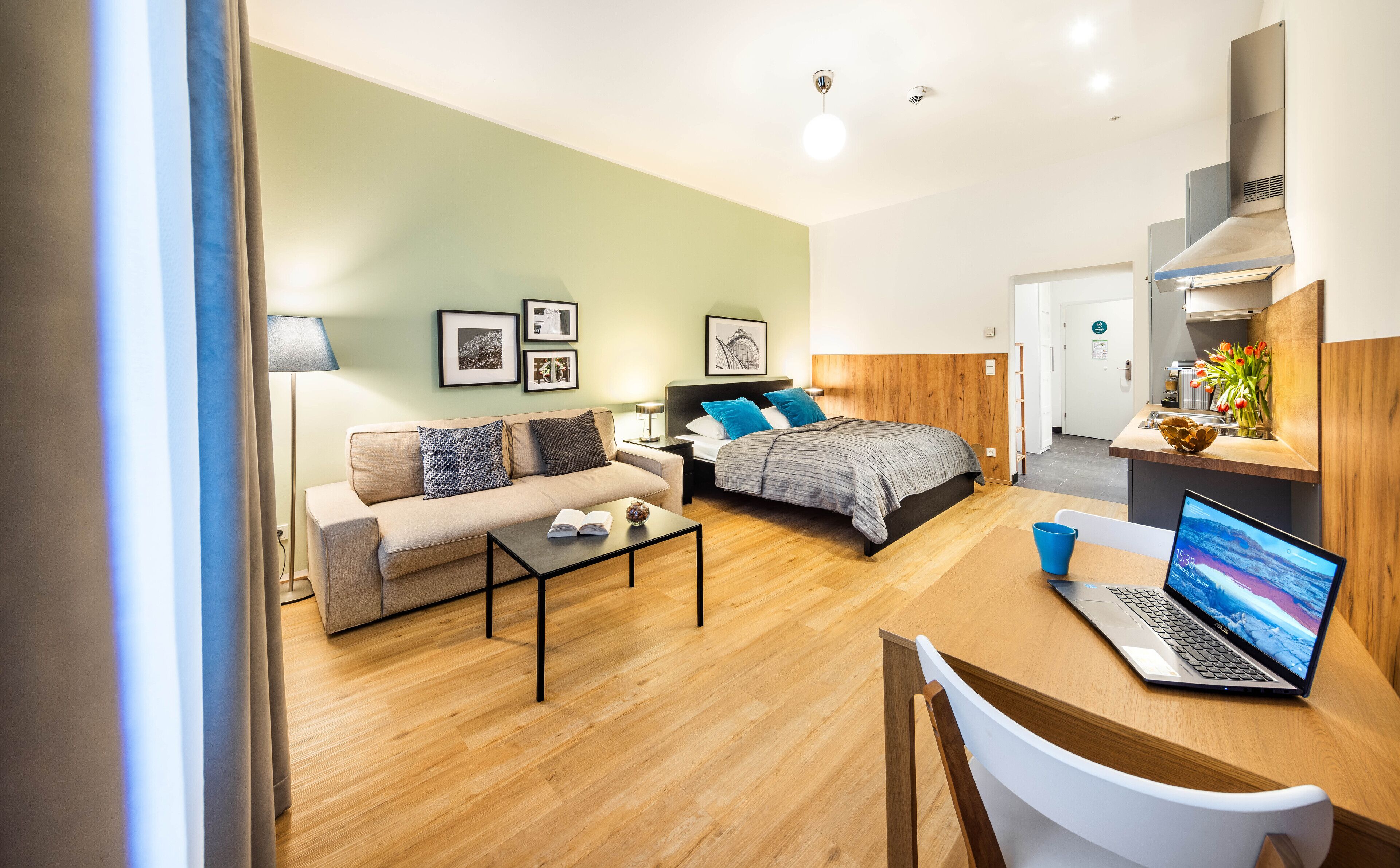 A modern hotel room with a bed, sofa, coffee table, and a laptop on a desk.