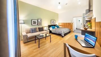A modern hotel room with a bed, sofa, coffee table, and a laptop on a desk.