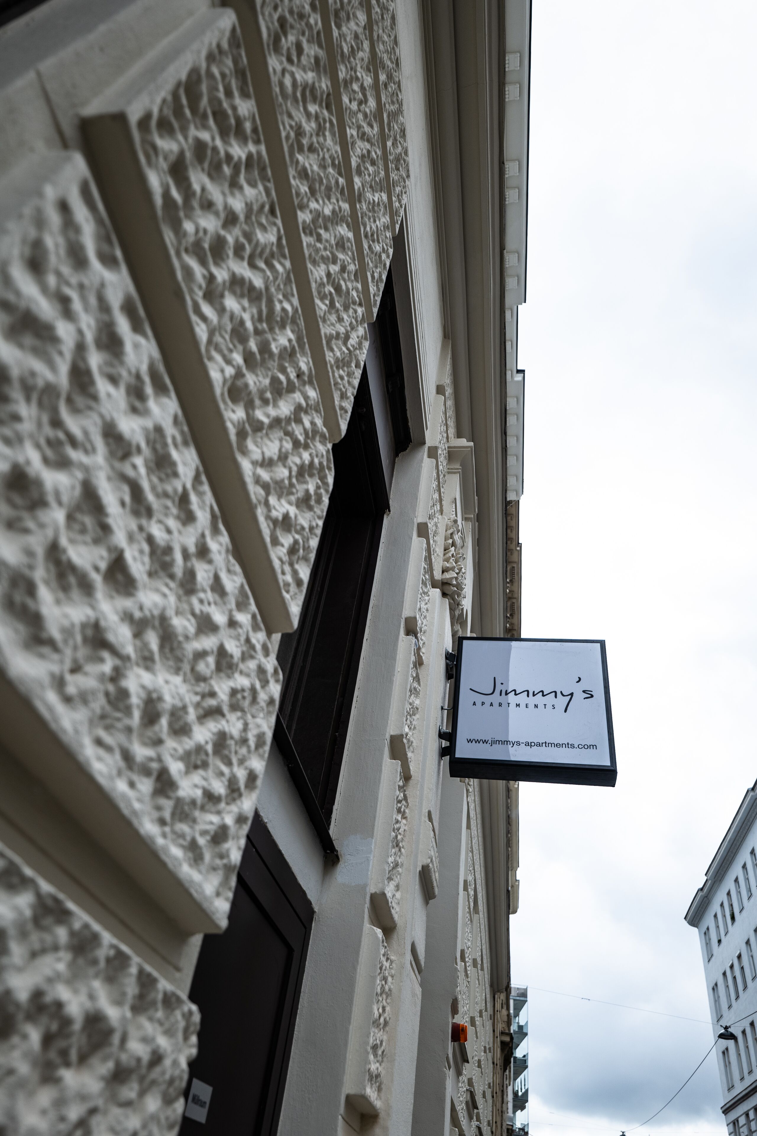 La façade d’un immeuble est recouverte d’un revêtement en pierre à texture et porte une enseigne indiquant « Appartements Jimmy ».