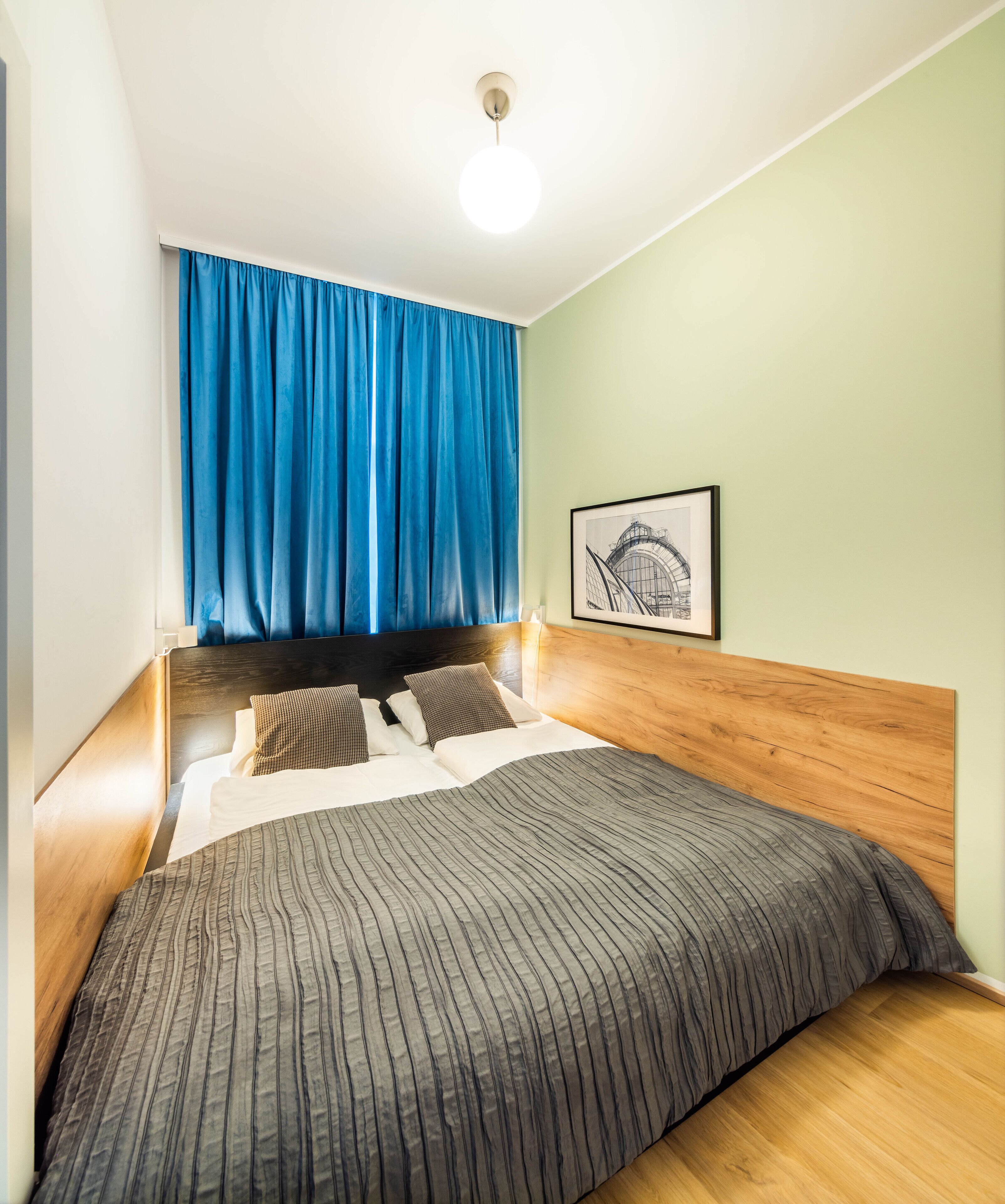 A neatly made bed with a striped bedspread, a wooden headboard, and a blue curtain.