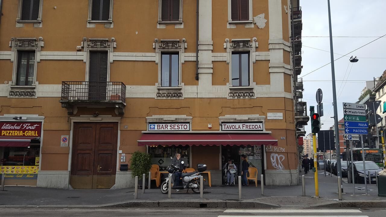 A building with a yellow facade, a closed door, and signs for 'BAR SESTO' and 'TAVOLA FREDDA'.
