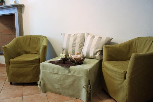 A cozy living room with two green armchairs and a small table with a basket of bread and a cup.