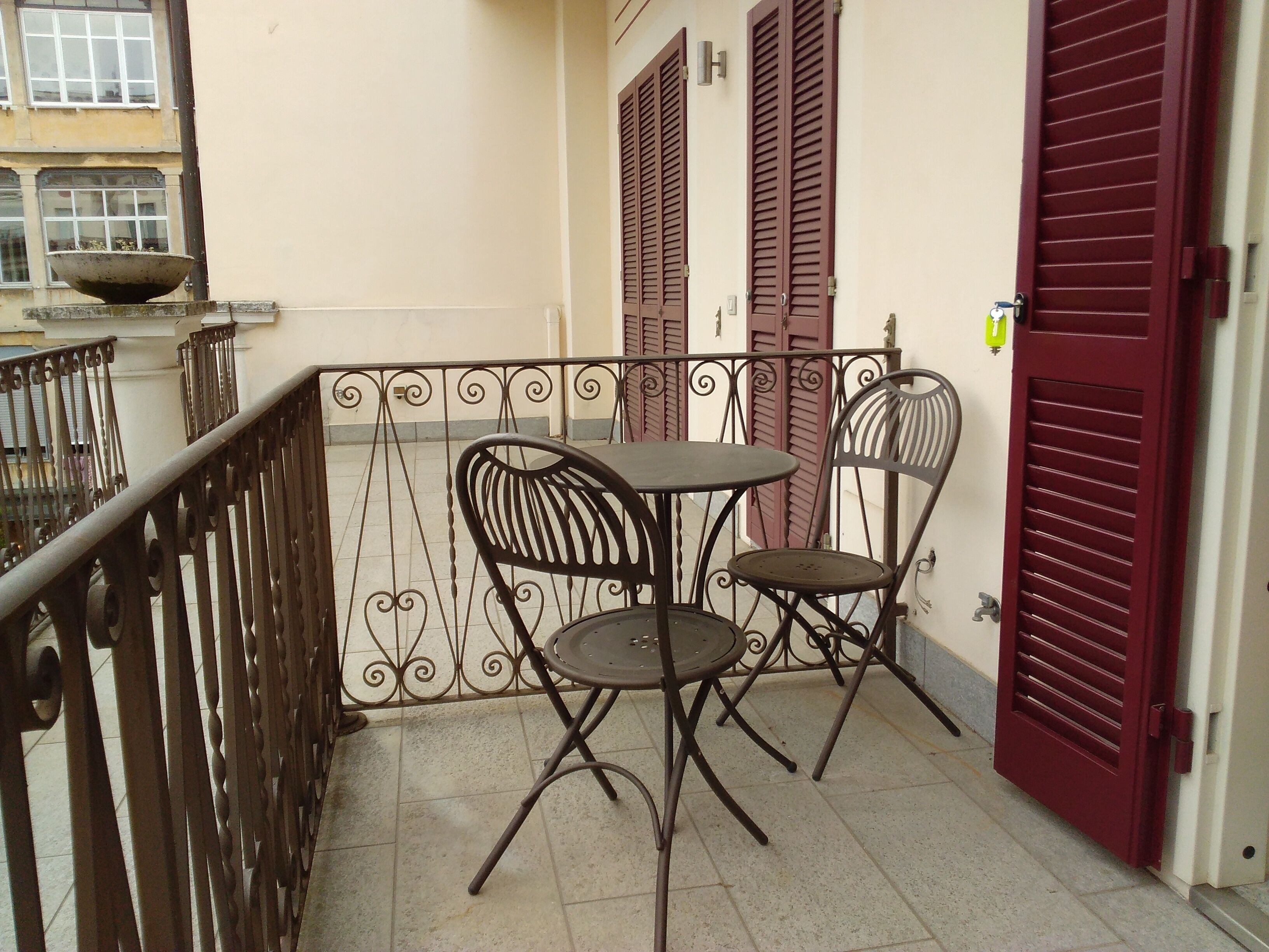 A balcony with a metal railing, a table with two chairs, and a red door.
