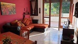 A living room with a sofa, a dining table with a plant, and a sliding glass door leading to a balcony. - Kibilù - Residenza del Parco Abete (Brebbia)