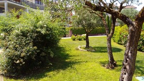 A well-maintained garden with various trees and shrubs, a clear pathway, and a building in the background. - Kibilù - Residenza del Parco Abete (Brebbia)