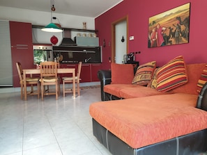 A living room with a sofa, chairs, a dining table, and a kitchen area with a stove and cabinets.