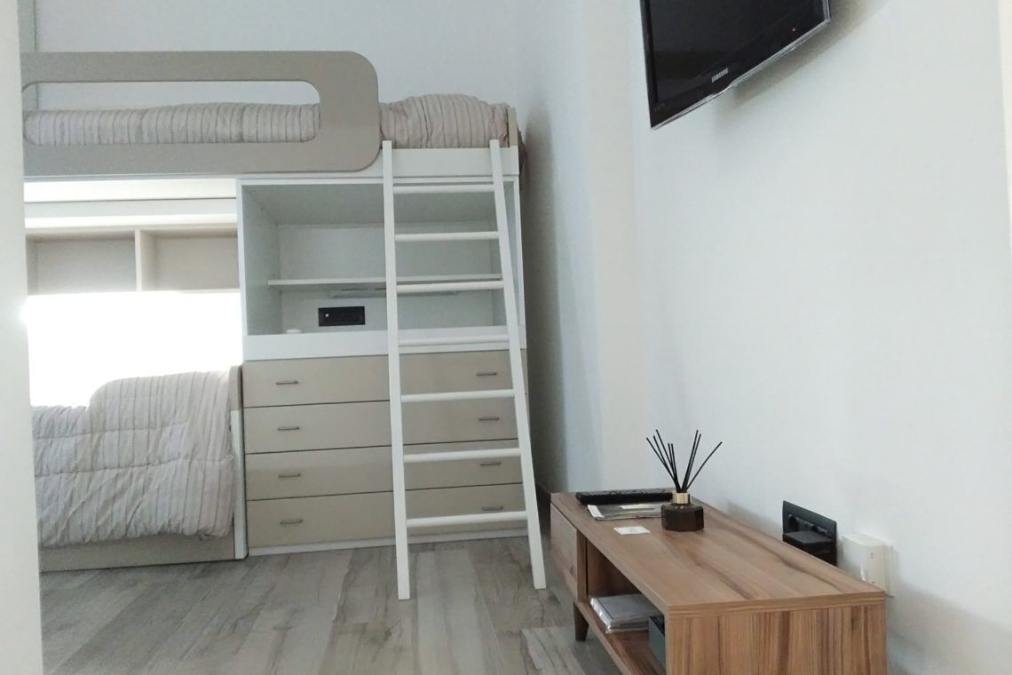 A bunk bed with a desk and a TV in a bedroom.