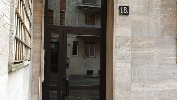 A building entrance with a glass door, a metal gate, and a number '18' sign. - Kibilù - Via Console Marcello (Milan)