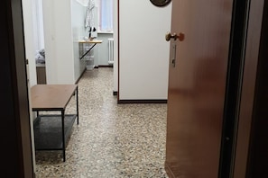 A hallway with a tiled floor leading to a room with a bed and a window.
